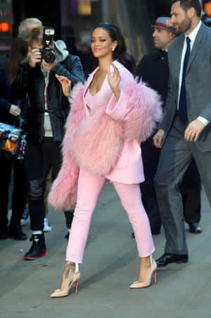 Rihanna 穿著粉紅色毛皮大衣和高跟鞋走在城市街道上。 — POCO Pad 壁紙