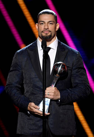 Roman Reigns 在彩色燈光下於舞台上手持 ESPY 獎項。 — 羅曼·雷恩斯 壁紙