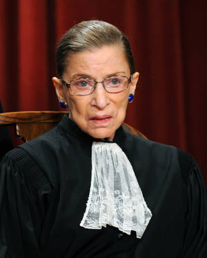 Ruth Bader Ginsburg 身穿法官袍，配蕾絲領飾和藍色耳環。 — 露絲·拜德·金斯伯格 壁紙