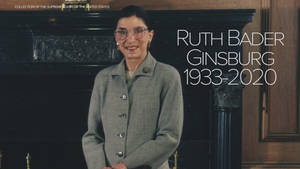 Ruth Bader Ginsburg 穿著灰色外套在壁爐前微笑，帶有文字疊加。 — 露絲·拜德·金斯伯格 壁紙