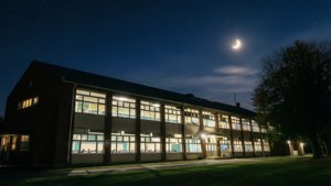 夜晚的學校建築，窗戶亮著燈，上方有一彎新月。