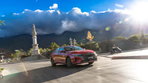 紅色轎車在明媚陽光下行駛在風景如畫的道路上，有石柱和山脈。