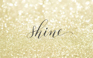 在金色亮粉背景上以草書寫的「shine」這個詞。 — 閃閃發光 壁紙