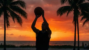 男子在沙灘上夕陽下棕櫚樹旁投籃