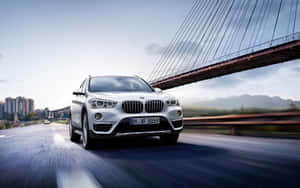 銀色BMW SUV在橋上高速行駛，背景有城市建築和山脈。 — Steam Deck OLED 壁紙