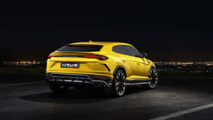 黃色藍寶堅尼 Urus SUV 夜間停泊，俯瞰城市景觀。 — 蘭博基尼 壁紙
