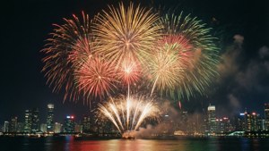 色彩繽紛的煙火在夜間水面上反射的城市天際線上方綻放。