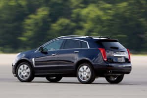 黑色Cadillac SRX SUV在道路上行駛，後面有綠色樹木。 — Surface Laptop 壁紙