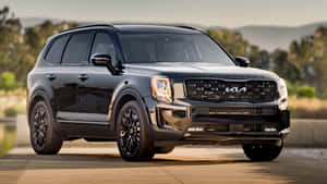 黑色Kia Telluride SUV在日落時停放在戶外，靠近山丘和樹木。 — 起亞 壁紙