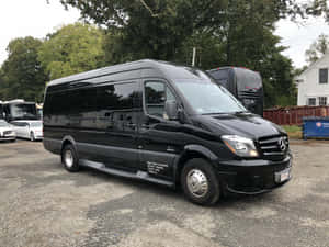 黑色 Mercedes-Benz Sprinter 客貨車停放在戶外碎石上，靠近樹木和其他車輛。 — 凱迪拉克 壁紙