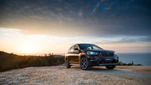 棕色BMW X1 SUV停泊在懸崖邊緣，日落時分俯瞰海洋。 — Mercedes Benz C300 壁紙