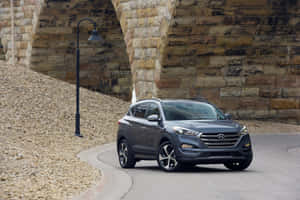 灰色Hyundai Tucson SUV在石橋下的碎石路上行駛。 — Surface Pro 壁紙