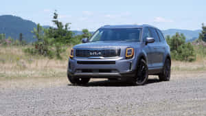 灰色Kia Telluride SUV停泊在碎石路上，背景有森林山丘。 — 起亞 壁紙
