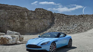 淺藍色Aston Martin跑車停泊在岩石地形附近，天空中有新月。 — 奧斯頓馬丁 壁紙