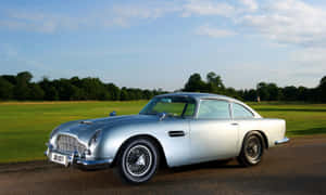銀色經典Aston Martin DB5停泊在日落時分靠近綠色田野的道路上。 — 奧斯頓馬丁 壁紙