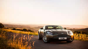 日落時分，銀色 Aston Martin 跑車行駛在風景如畫的鄉村道路上。 — 奧斯頓馬丁 壁紙