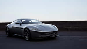 銀色Aston Martin跑車停泊在瀝青路上，靠近混凝土護欄。 — 奧斯頓馬丁 壁紙