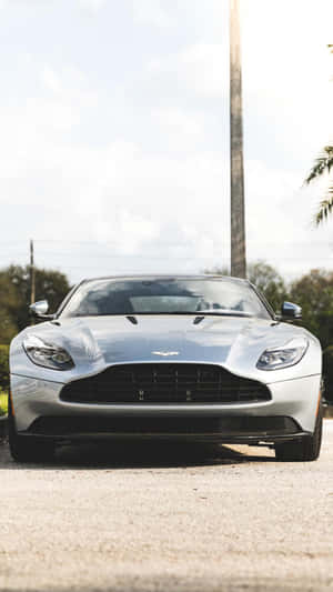銀色Aston Martin跑車停泊在碎石路上，有棕櫚樹和電線桿。 — 奧斯頓馬丁 壁紙