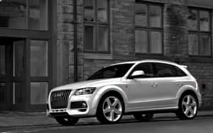 銀色Audi Q7 SUV停放在城市街道旁的石造建築物旁。 — Steam Deck 壁紙