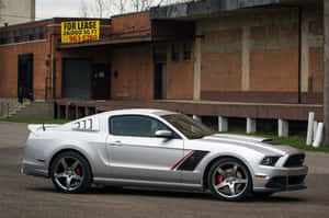 銀色福特野馬停在磚砌建築前，帶有「出租」標誌。 — 野馬GIF 壁紙