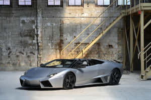 銀色藍寶堅尼 Reventon Roadster 在一個有黃色金屬樓梯的工業倉庫內。 — Surface Pro 壁紙