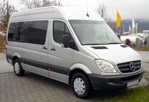銀色 Mercedes-Benz Sprinter 客貨車停放在鋪砌的停車場，靠近樹木和山脈。 — Mercedes-Benz 壁紙