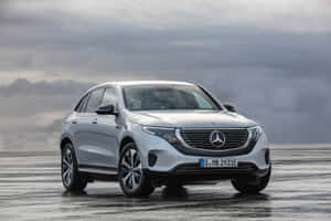 銀色 Mercedes EQC 電動 SUV 在潮濕道路上行駛，天空多雲 — Mercedes-Benz 壁紙