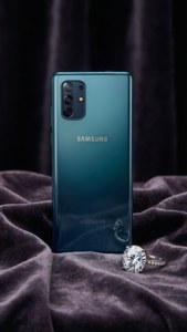 深色天鵝絨布料上的青色Samsung手機和鑽石戒指。