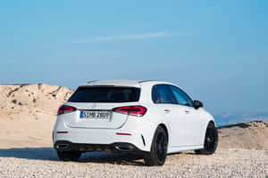 白色 Mercedes-Benz A-Class 掀背車在礫石上，有山和藍天。 — Mercedes-Benz 壁紙