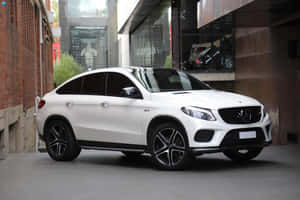 白色賓士 GLE Coupe 停放在城市小巷中，位於磚牆和玻璃建築之間。 — MacBook Air 壁紙