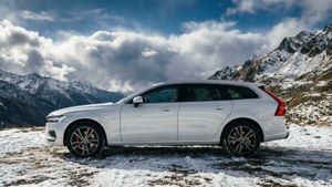 白色旅行車停放在雪地山景中，天空多雲。