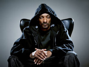 Snoop Dogg 身穿黑色連帽衫坐在皮椅上，戴著銀色耳環，手部纏著繃帶。 — 史努比狗狗 壁紙