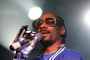 Snoop Dogg 在舞台上戴著太陽眼鏡和白色手套對著麥克風唱歌。 — 史努比狗狗 壁紙