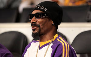 Snoop Dogg 在體育活動中穿著湖人裝備，戴著太陽眼鏡和毛帽。 — 史努比狗狗 壁紙