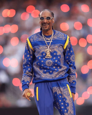 Snoop Dogg 身穿藍色佩斯利花紋運動服，在舞台上微笑，身後有紅色燈光。 — 羅賓漢 壁紙