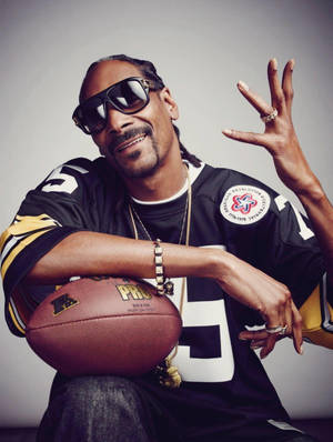 Snoop Dogg 身穿美式足球球衣，手持足球並揮手。 — 史努比狗狗 壁紙