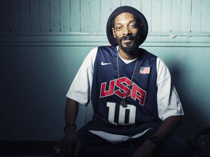 Snoop Dogg 身穿美國籃球球衣和毛帽，對著藍色牆壁微笑。 — 史努比狗狗 壁紙