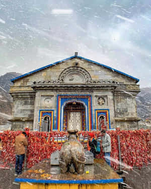 雪落在有紅色經幡的寺廟上，人們靠近公牛雕像。 — 廟宇 壁紙