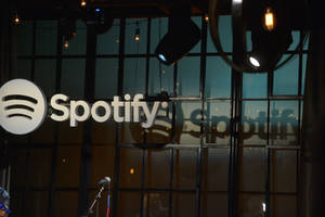 Spotify 標誌顯示在玻璃牆上，配有舞台燈光和麥克風。 — Spotify 壁紙