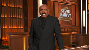 Steve Harvey 在電視節目場景中穿著黑色西裝微笑。 — 比利·哈格羅夫 壁紙
