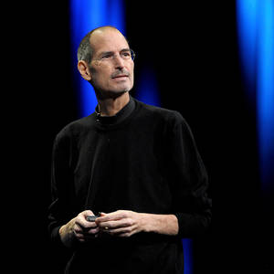 Steve Jobs 在藍色燈光的舞台上手持裝置。 — 蘋果 壁紙