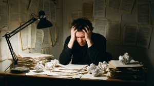 一個沮喪的作家，書桌周圍滿是皺巴巴的紙張和一堆堆文件。