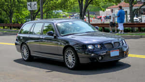 黑色MG ZT Tourer旅行車停在綠樹成蔭的街道上，附近有人。 — 凱迪拉克 壁紙