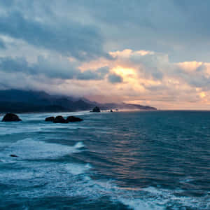 海岸日落，海浪拍打岩石，山巒在霧中。 — 海灘日落 壁紙