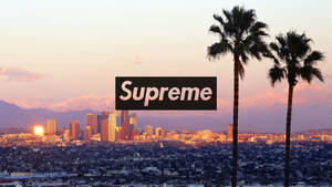 Supreme 標誌在城市上空，有棕櫚樹和山脈的日落景色 — 酷炫至尊 壁紙