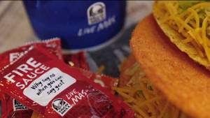 Taco Bell 火辣醬包和起司玉米餅，附有一個飲料杯。 — 塔可 壁紙
