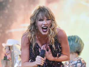 Taylor Swift 在舞台上穿著閃亮黑色連衣裙，金色頭髮唱歌。 — 泰勒絲 壁紙
