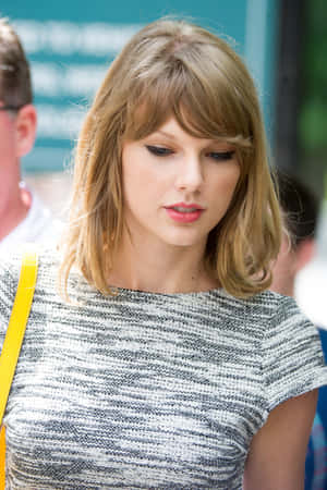 Taylor Swift 身穿灰色質感上衣，搭配黃色肩帶手袋，在戶外。 — 泰勒絲 壁紙