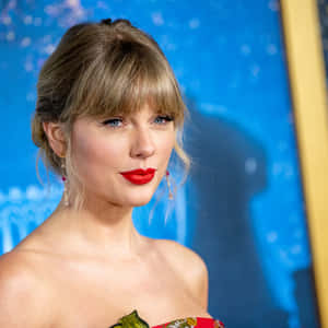 Taylor Swift 身穿紅色連衣裙，塗著大膽的紅色唇膏，在藍色活動背景下。 — 泰勒絲 壁紙