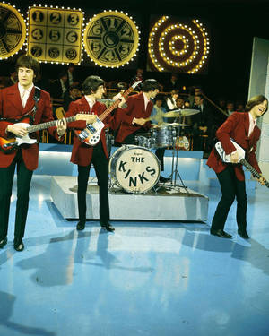 The Kinks 樂團在藍色舞台上現場表演，身後有時鐘燈光。 — 岩石 壁紙